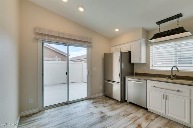 kitchen featuring a healthy amount of sunlight, lofted ceiling, a sink, stainless steel appliances, and dark countertops