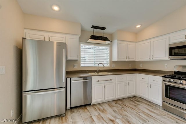 kitchen with a sink, light wood-type flooring, dark countertops, and appliances with stainless steel finishes