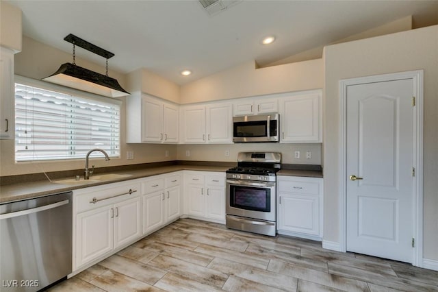 kitchen featuring dark countertops, vaulted ceiling, stainless steel appliances, and a sink