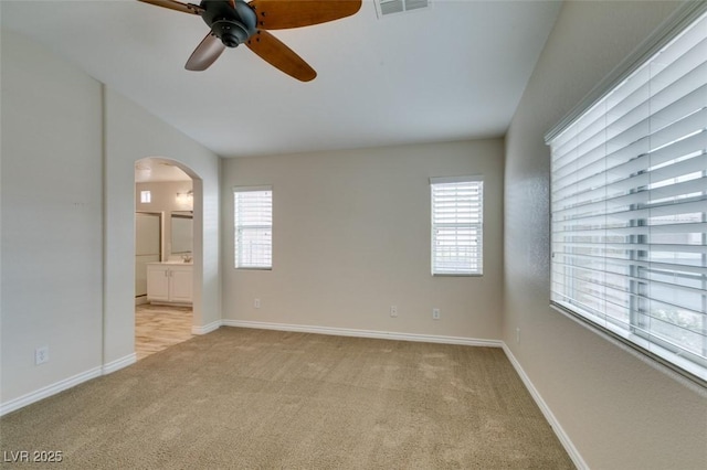 spare room with a ceiling fan, baseboards, visible vents, arched walkways, and light carpet