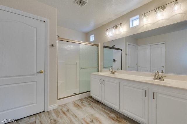 full bathroom with visible vents, a stall shower, a sink, and wood finished floors