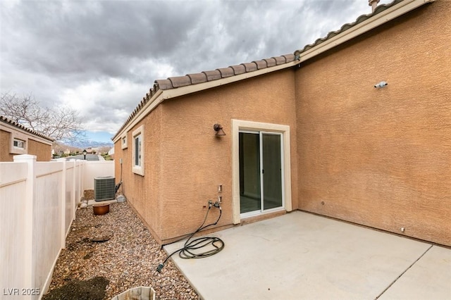 rear view of property with stucco siding, a tiled roof, central AC, fence, and a patio area