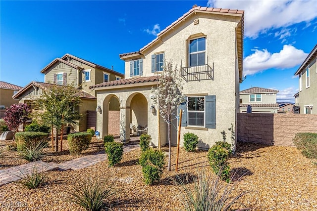 mediterranean / spanish home featuring stucco siding, a tile roof, and fence