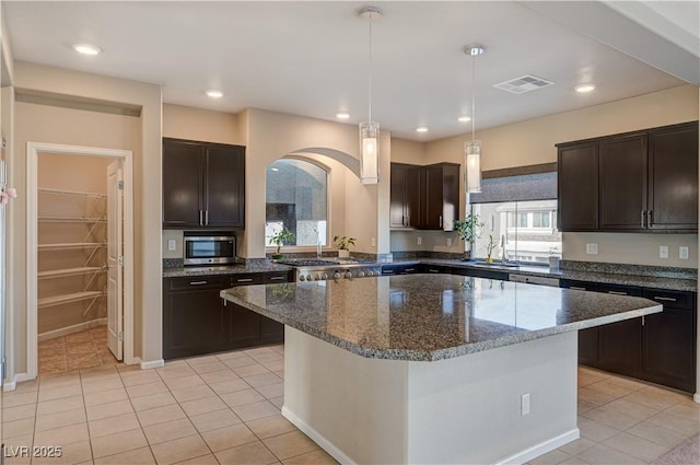 kitchen with stainless steel microwave, visible vents, dark brown cabinetry, dark stone countertops, and a sink