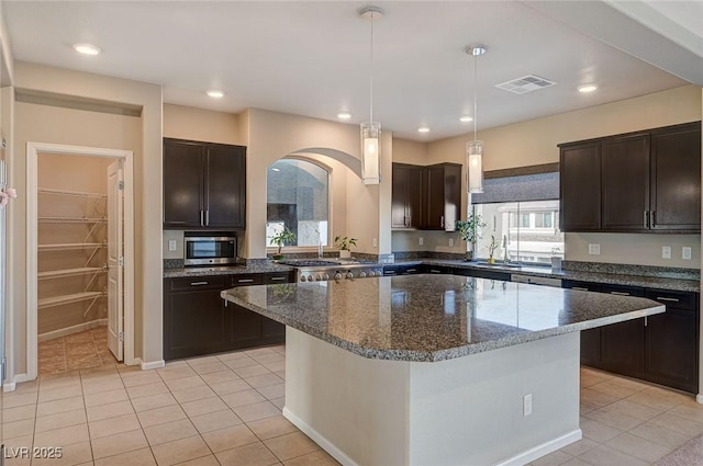 kitchen featuring stainless steel microwave, light tile patterned floors, visible vents, and dark brown cabinetry