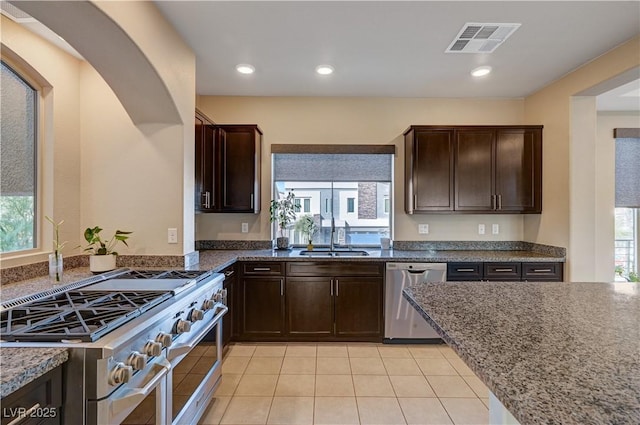 kitchen featuring visible vents, dark brown cabinetry, dark stone countertops, appliances with stainless steel finishes, and a sink