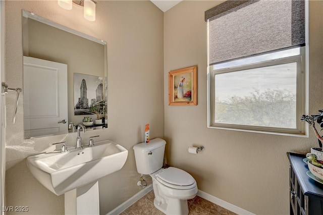 half bath featuring tile patterned flooring, toilet, baseboards, and a sink