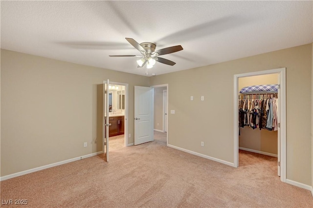 unfurnished bedroom with light carpet, a closet, a walk in closet, and baseboards