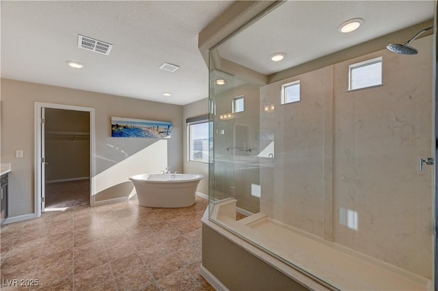 full bathroom featuring visible vents, a walk in closet, a shower stall, baseboards, and a freestanding bath