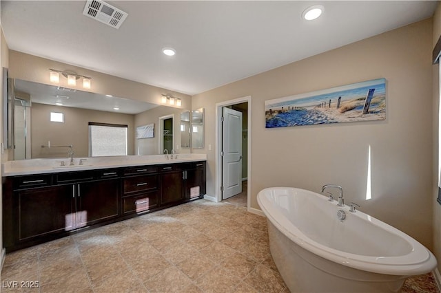 bathroom with baseboards, visible vents, double vanity, a freestanding bath, and a sink