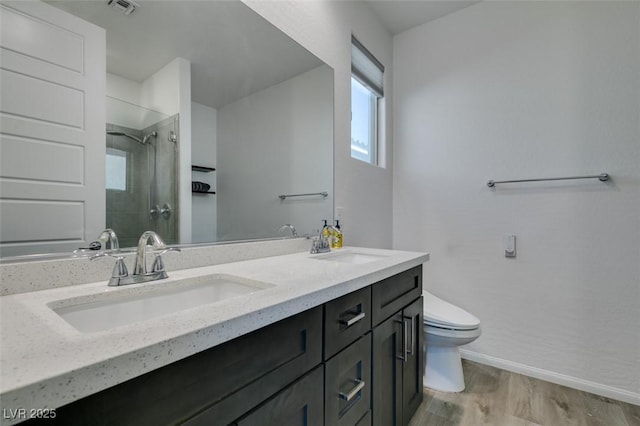 bathroom with wood finished floors, toilet, tiled shower, and a sink