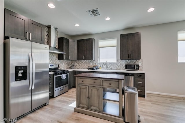 kitchen with stainless steel appliances, light countertops, dark brown cabinets, wall chimney exhaust hood, and tasteful backsplash