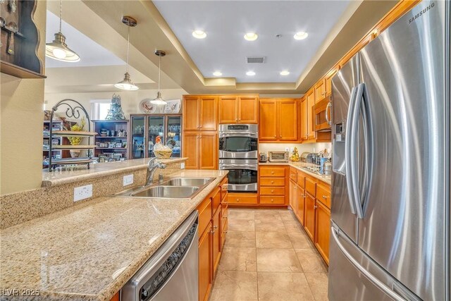 64 Strada Principale Unit 307, Henderson, NV 89011 - kitchen featuring stainless steel appliances, a sink, hanging light fixtures, a raised ceiling, and brown cabinetry