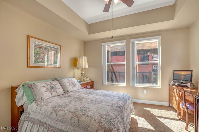 carpeted bedroom with a tray ceiling, baseboards, and ceiling fan