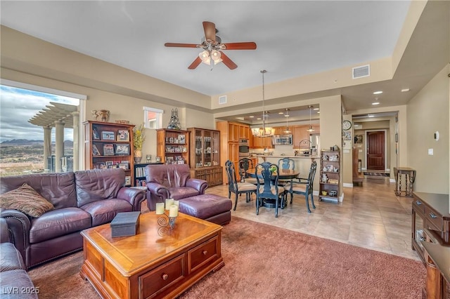 living room with light tile patterned floors, visible vents, recessed lighting, ceiling fan with notable chandelier, and light colored carpet