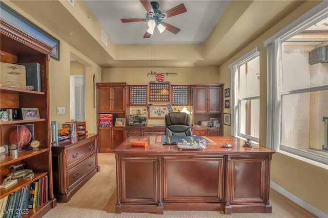 home office featuring visible vents, a ceiling fan, baseboards, a raised ceiling, and light colored carpet