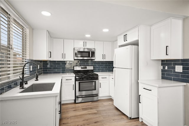 kitchen with light wood finished floors, a sink, stainless steel appliances, white cabinets, and light countertops