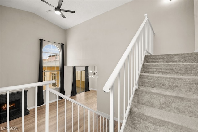 staircase featuring lofted ceiling, ceiling fan with notable chandelier, wood finished floors, a fireplace, and baseboards