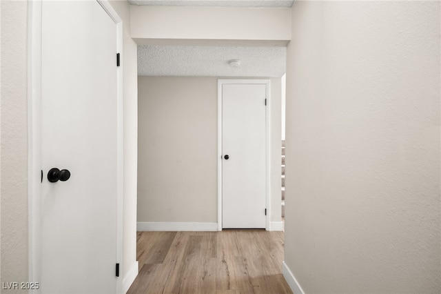 corridor featuring a textured ceiling, baseboards, and wood finished floors