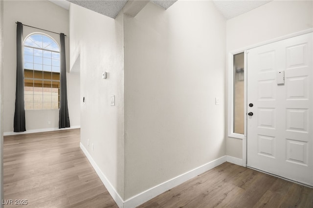 foyer entrance with baseboards, a textured ceiling, and wood finished floors