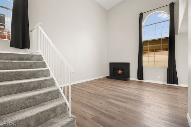 staircase featuring a fireplace, a high ceiling, wood finished floors, and baseboards