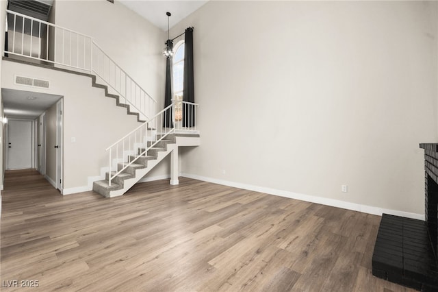 unfurnished living room with visible vents, baseboards, stairs, a high ceiling, and wood finished floors