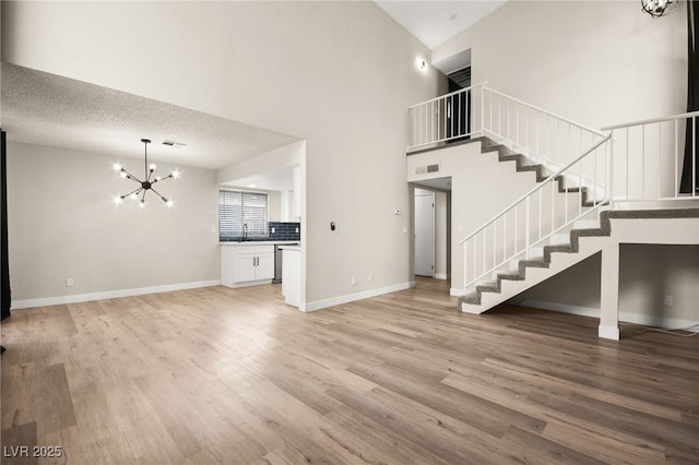 unfurnished living room with light wood-type flooring, baseboards, an inviting chandelier, and stairs