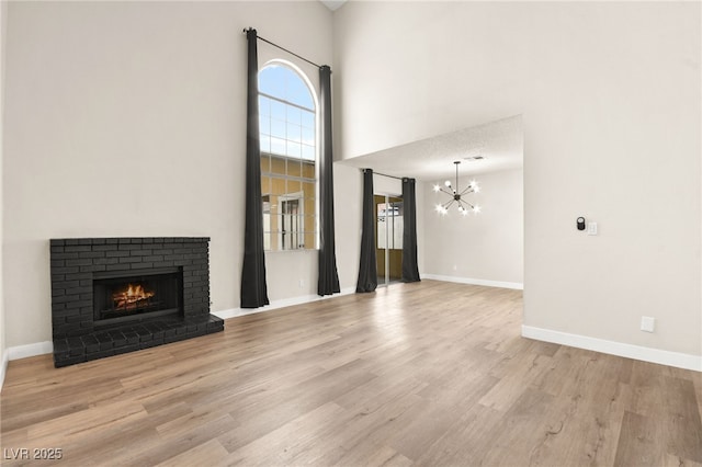 unfurnished living room featuring baseboards, wood finished floors, a fireplace, a towering ceiling, and an inviting chandelier