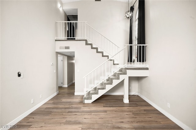 staircase with visible vents, baseboards, a towering ceiling, and wood finished floors