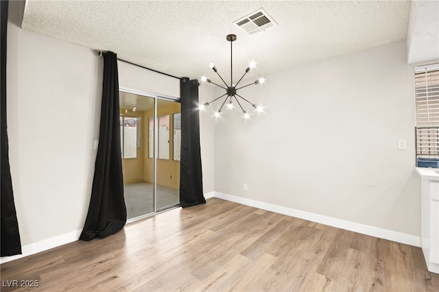 unfurnished dining area with baseboards, visible vents, a textured ceiling, light wood-type flooring, and a chandelier