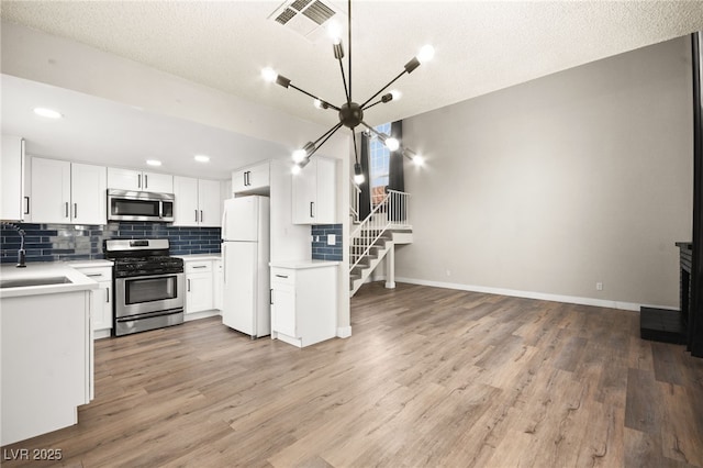 kitchen with a sink, decorative backsplash, light countertops, appliances with stainless steel finishes, and light wood-type flooring