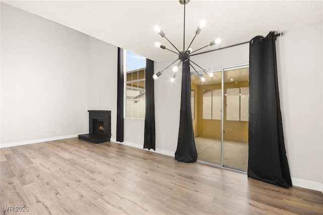 unfurnished living room featuring a brick fireplace, baseboards, an inviting chandelier, and wood finished floors