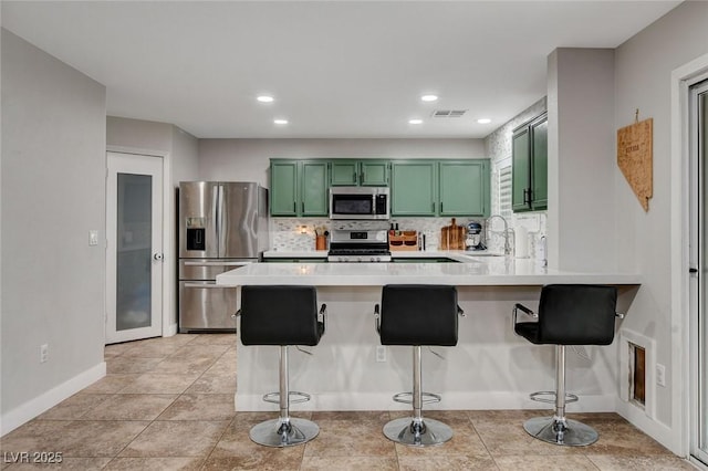 kitchen featuring a peninsula, light countertops, appliances with stainless steel finishes, green cabinets, and backsplash