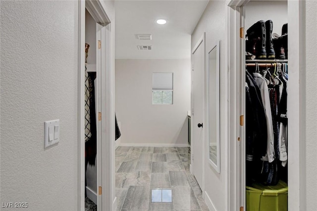 corridor featuring visible vents, baseboards, and a textured wall