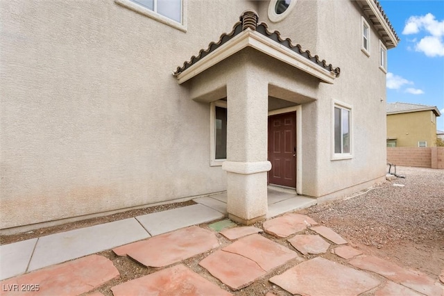 doorway to property featuring stucco siding, a tile roof, and fence