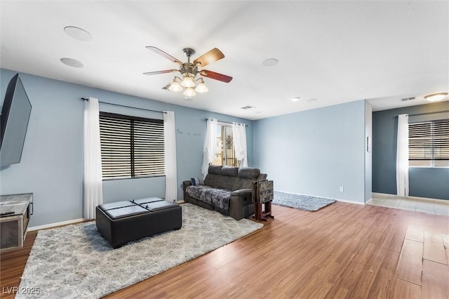 living room featuring visible vents, baseboards, wood finished floors, and a ceiling fan