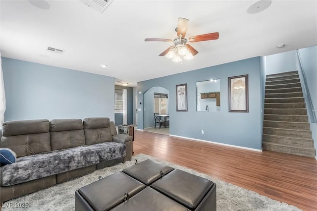 living area with stairway, wood finished floors, visible vents, arched walkways, and ceiling fan