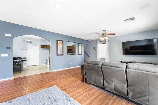 living room featuring visible vents, a ceiling fan, arched walkways, light wood finished floors, and baseboards