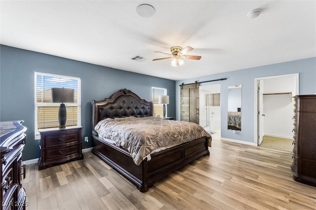 bedroom featuring a barn door, light wood-style flooring, baseboards, and visible vents