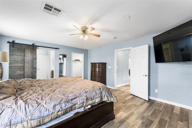 bedroom featuring visible vents, baseboards, a barn door, wood finished floors, and a ceiling fan