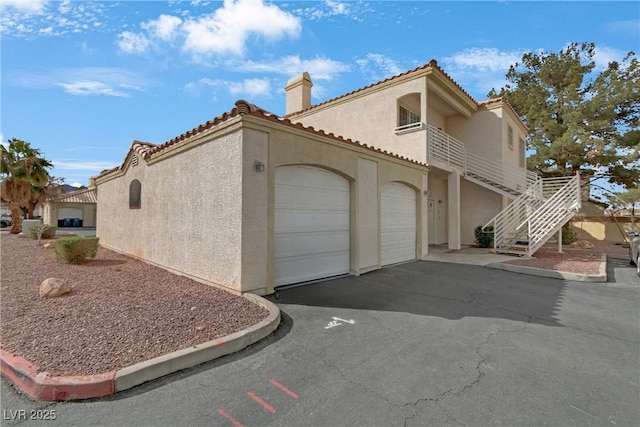 view of side of home featuring aphalt driveway, a tile roof, stairs, stucco siding, and a chimney