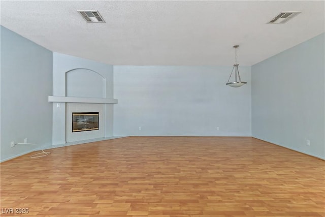 unfurnished living room featuring visible vents, light wood-style flooring, a tile fireplace, and a textured ceiling