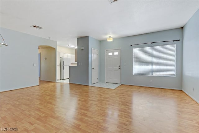 unfurnished living room with light wood-style flooring, arched walkways, visible vents, and baseboards