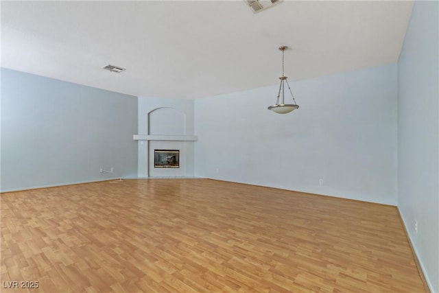 unfurnished living room featuring a glass covered fireplace, visible vents, and light wood-style flooring