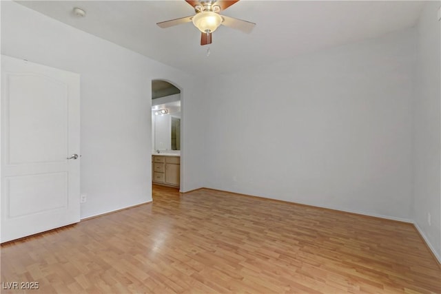 unfurnished room featuring light wood-style flooring, a ceiling fan, and arched walkways