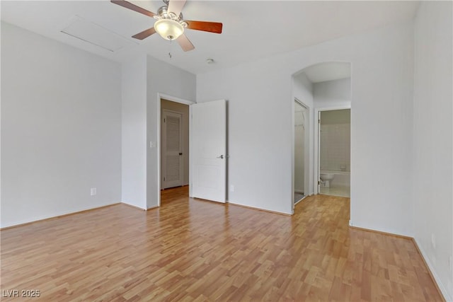 spare room with a ceiling fan, arched walkways, light wood finished floors, and baseboards