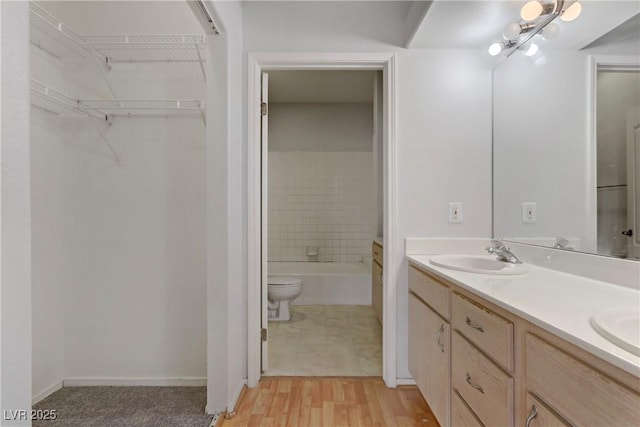 bathroom with wood finished floors, double vanity, a tub, a sink, and a walk in closet