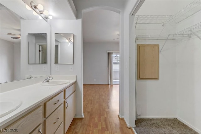 bathroom with wood finished floors, baseboards, double vanity, ceiling fan, and a sink