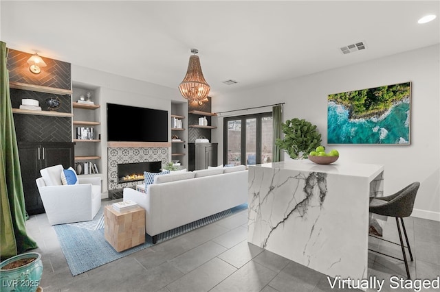 tiled living area featuring a notable chandelier, visible vents, a fireplace, and built in features