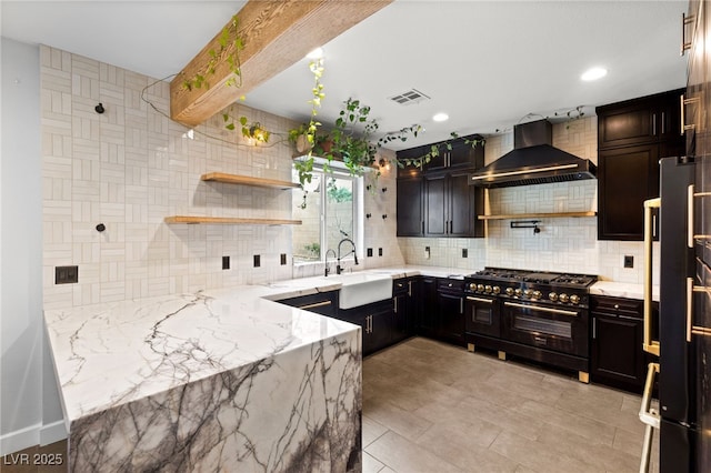 kitchen featuring visible vents, light stone counters, a sink, wall chimney range hood, and range with two ovens